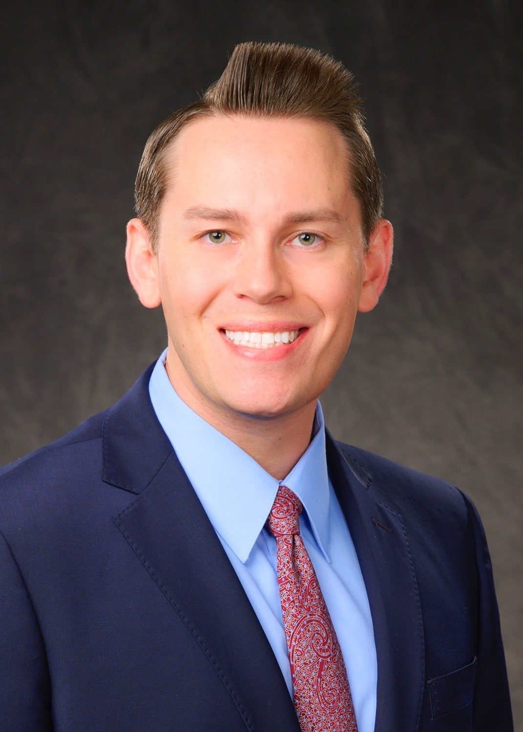 Attorney Alexander Bowen of Williams Law Association, P.A. smiling in a professional headshot wearing a navy suit, light blue shirt, and red patterned tie against a dark background.